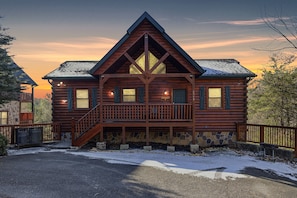 Une cabane en rondins avec des fondations en pierre, une terrasse en bois et un escalier menant à l’entrée.