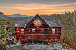 A log cabin with a balcony, a stone foundation, and a view of the mountains. - Knotty But Nice 4 Bedroom Home (Sevierville)