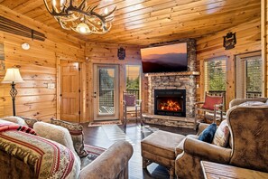 Un intérieur chaleureux de chalet en bois, avec une cheminée en pierre, des sièges confortables et un grand écran de télévision.
