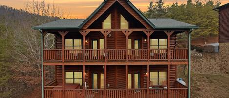 A multi-story log cabin with a stone foundation, balconies, and large windows.