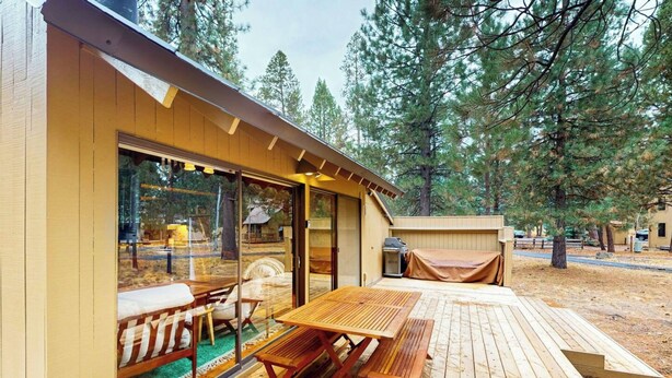 A wooden deck with picnic tables and a covered grill area, surrounded by trees. - 2BR Getaway with WiFi, Grill & SHARC Passes (Sunriver)