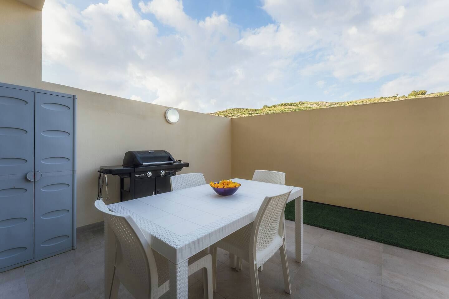 A patio with a table, chairs, a grill, and a view of the sky.