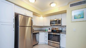 A modern kitchen with stainless steel appliances, white cabinetry, and a tiled floor.