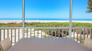 A balcony with a table and chairs overlooking a beach and ocean. - Beach Villa 2007 - beautifully renovated one-bedroom, one-bathroom condo (Captiva)