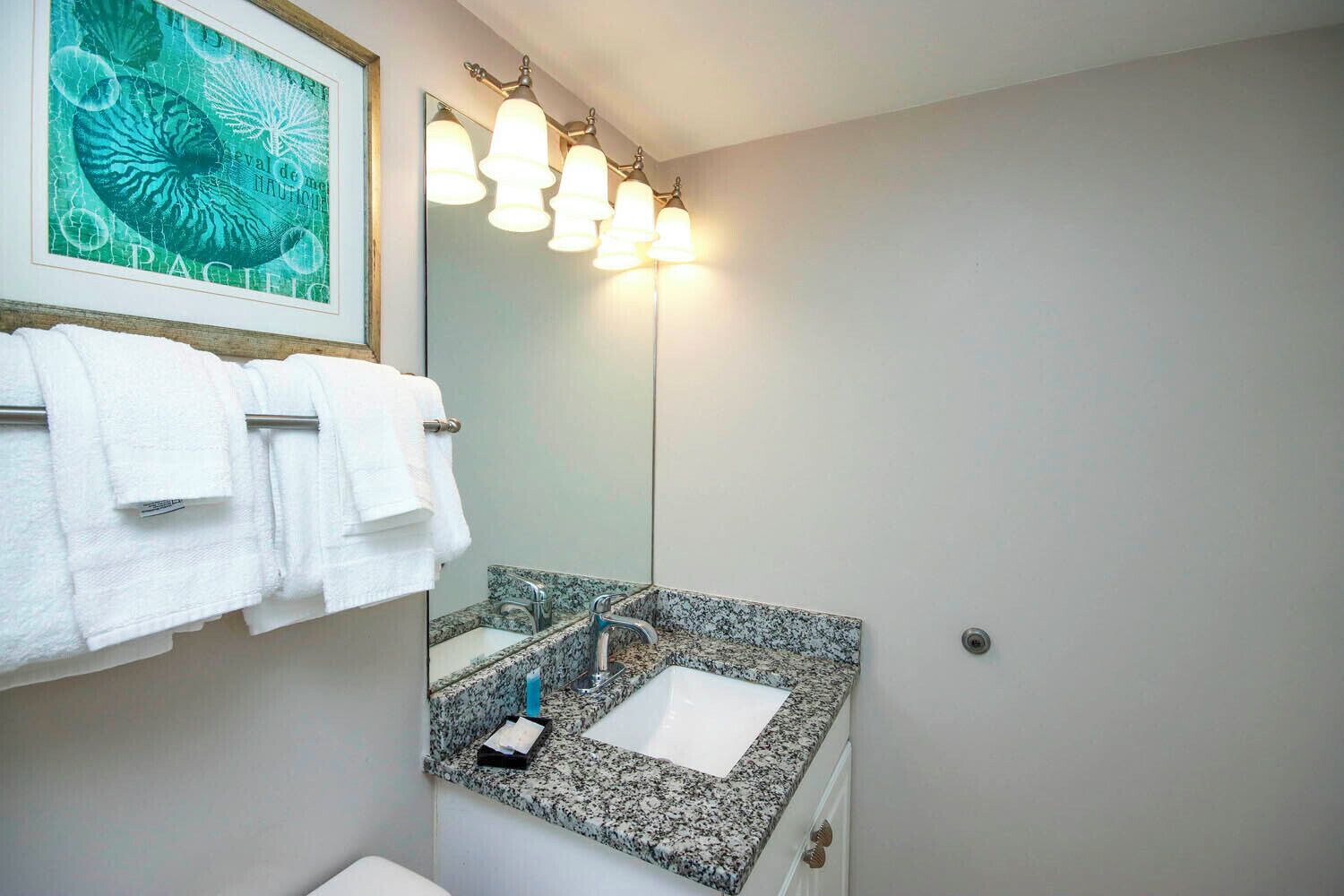 Une salle de bain avec un lavabo doté d’un plan de travail en granit, un grand miroir et un porte-serviettes avec des serviettes blanches.