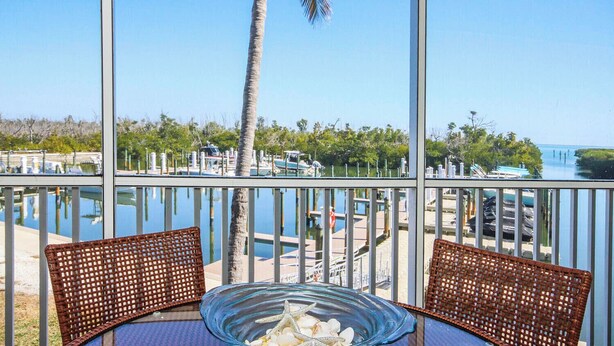 A view from a balcony with two wicker chairs and a glass table with seashells. - Bayside Villa 4108: Renovated Luxury & Spacious Comfort in the Heart of Captiva (Captiva)