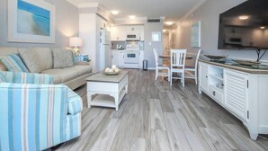 A modern living room with a sofa, striped armchair, coffee table, and dining area with chairs and a TV. - Bayside Villa 4108: Renovated Luxury & Spacious Comfort in the Heart of Captiva (Captiva)