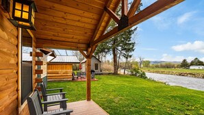Une cabane en bois avec une véranda, un espace salon extérieur et une vue sur une rivière.