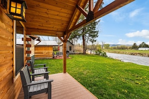 A wooden cabin with a porch, outdoor seating, and a view of a river.