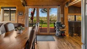 L’intérieur d’un chalet en bois, avec une table à manger, des chaises, un lustre et une vue à travers les portes vitrées.