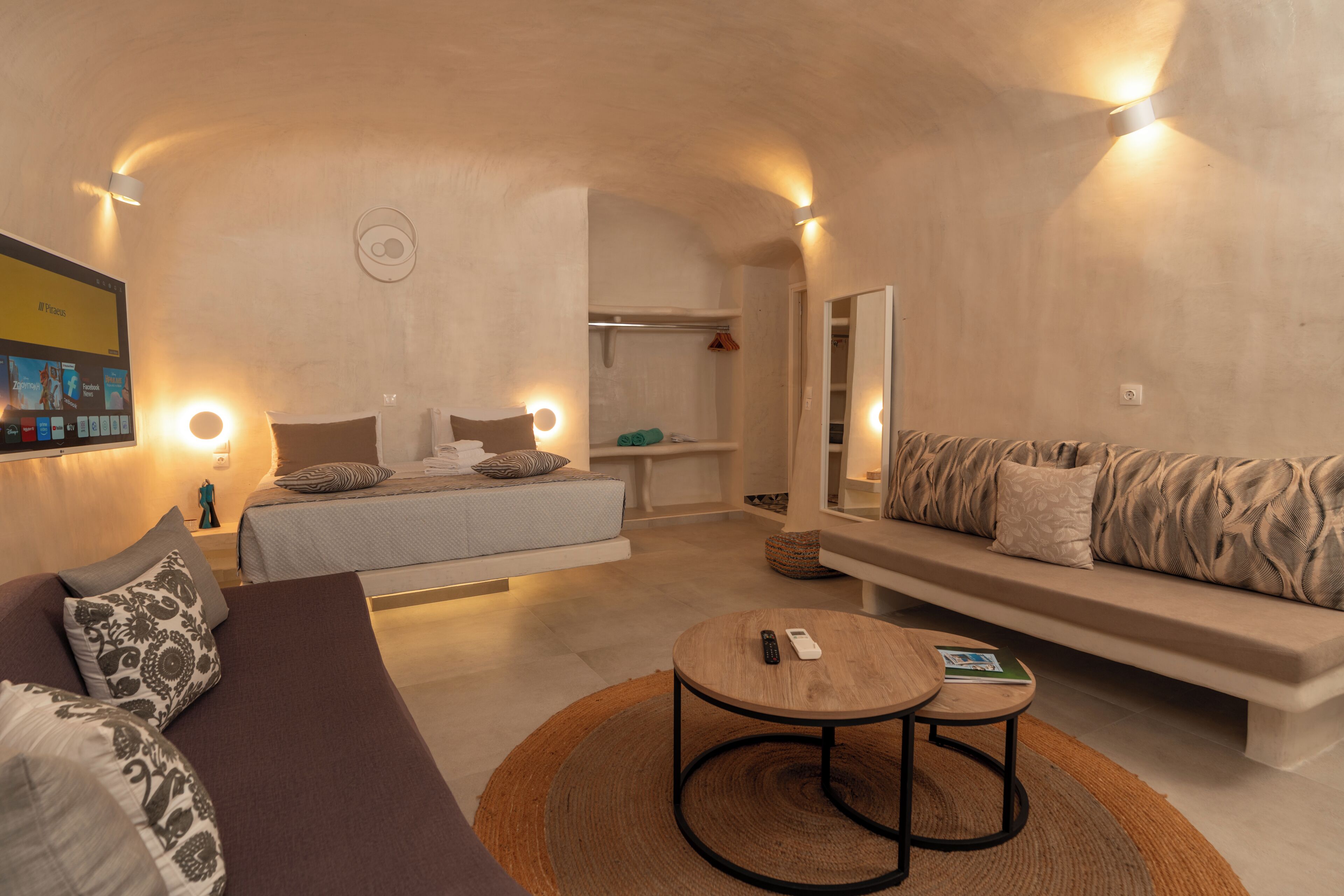 Ein modernes Hotelzimmer mit Sofa, rundem Tisch, Bett, Kleiderschrank und Spiegel.