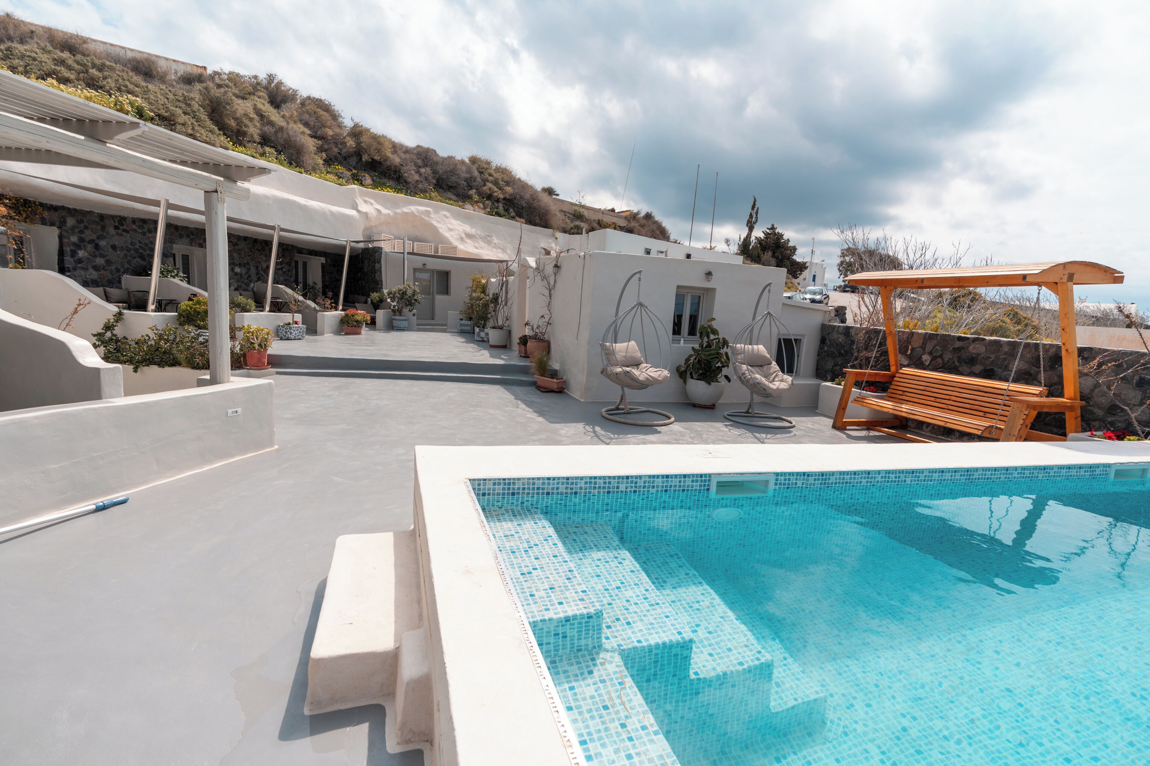 A pool area with a clear blue pool, outdoor seating, and a covered patio.