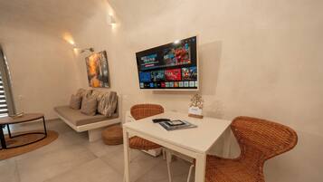 Una sala de estar moderna con un televisor de pantalla plana, un sofá, una mesa de comedor, sillas de mimbre y una pequeña planta decorativa.