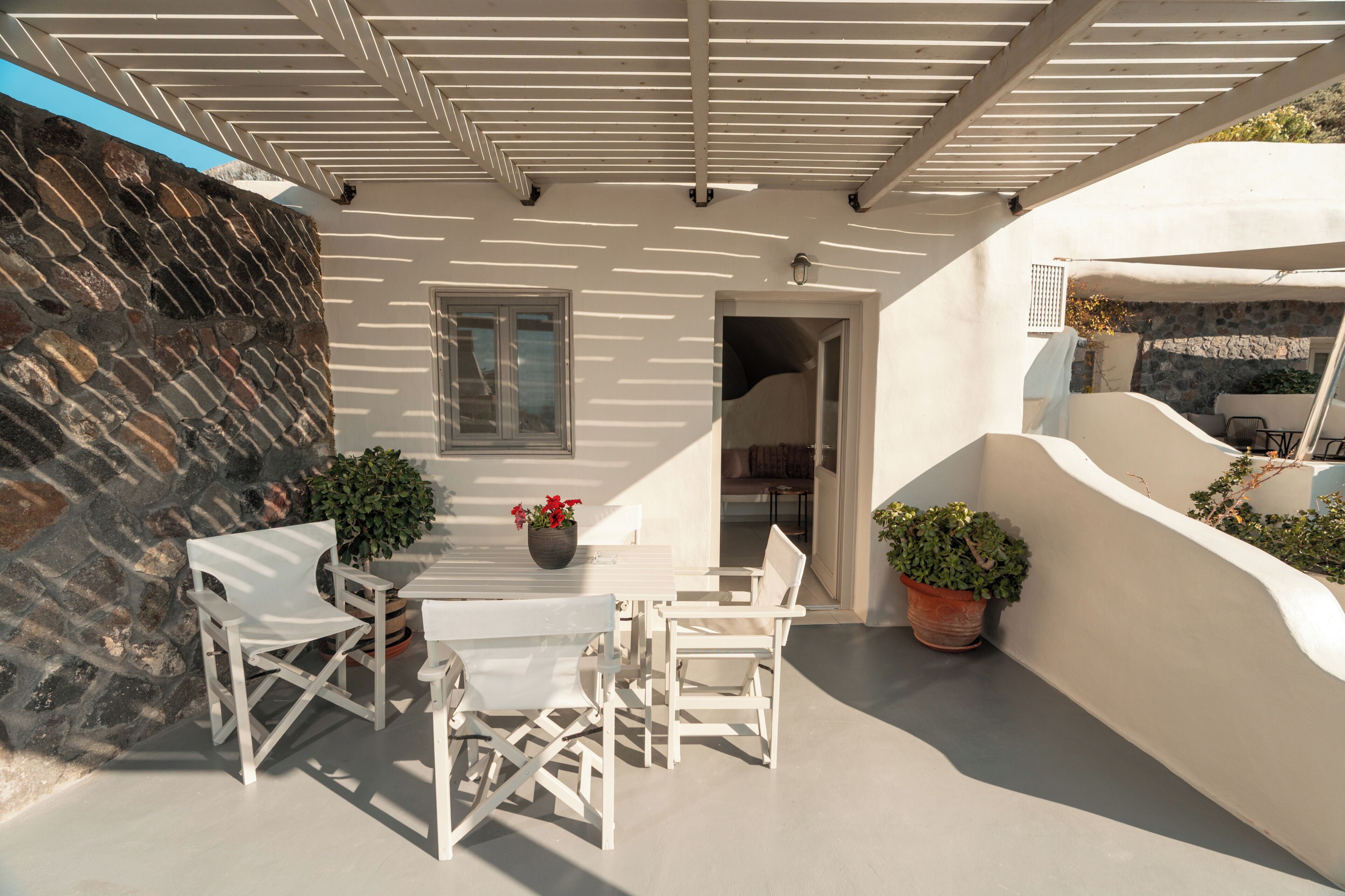 A covered outdoor seating area with white furniture, a stone wall, and potted plants.