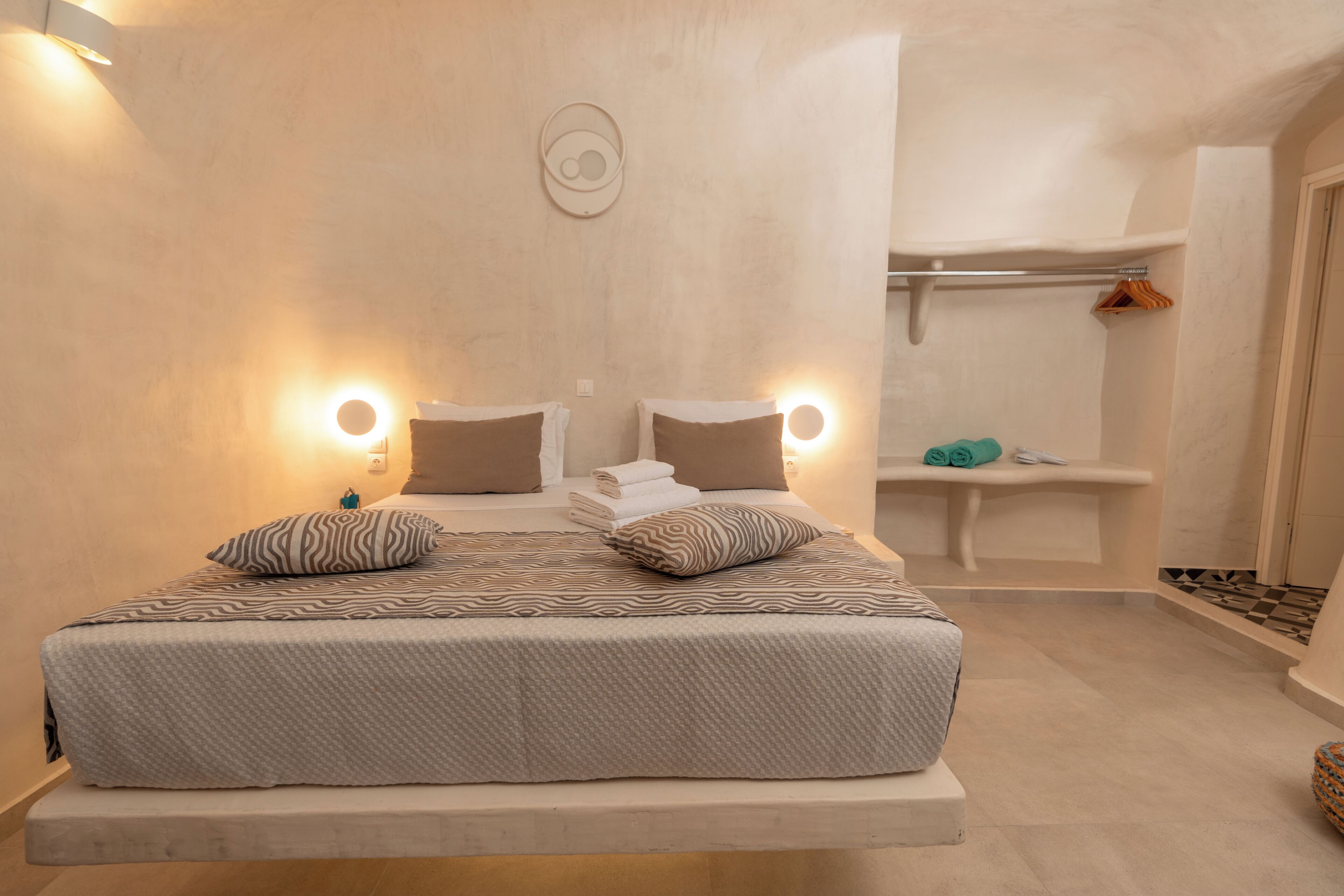 Un dormitorio con cama, lámparas de noche, un reloj de pared y un baño con perchero.