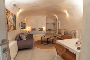 A modern interior with a sofa, dining table, and chairs, a small round table with a remote, and a painting on the wall. - Rody Caves Oia (Oia)