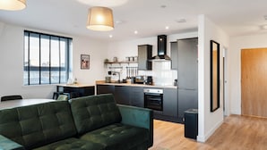 Un salon moderne avec un canapé vert, une table à manger et un coin cuisine doté d’un four encastré et d’un réfrigérateur.