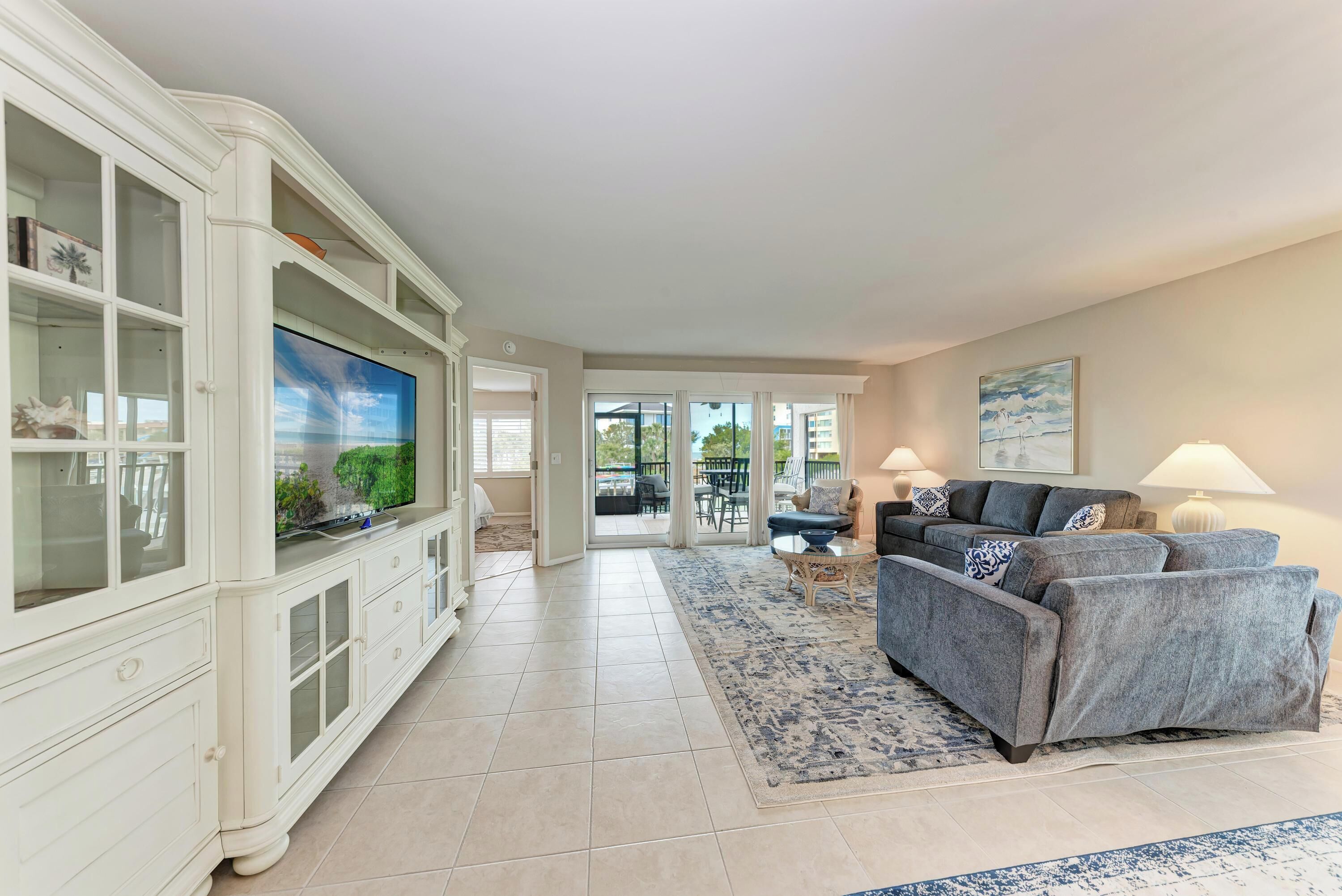 A spacious living room with a large TV, a grey sofa, and a white entertainment unit.