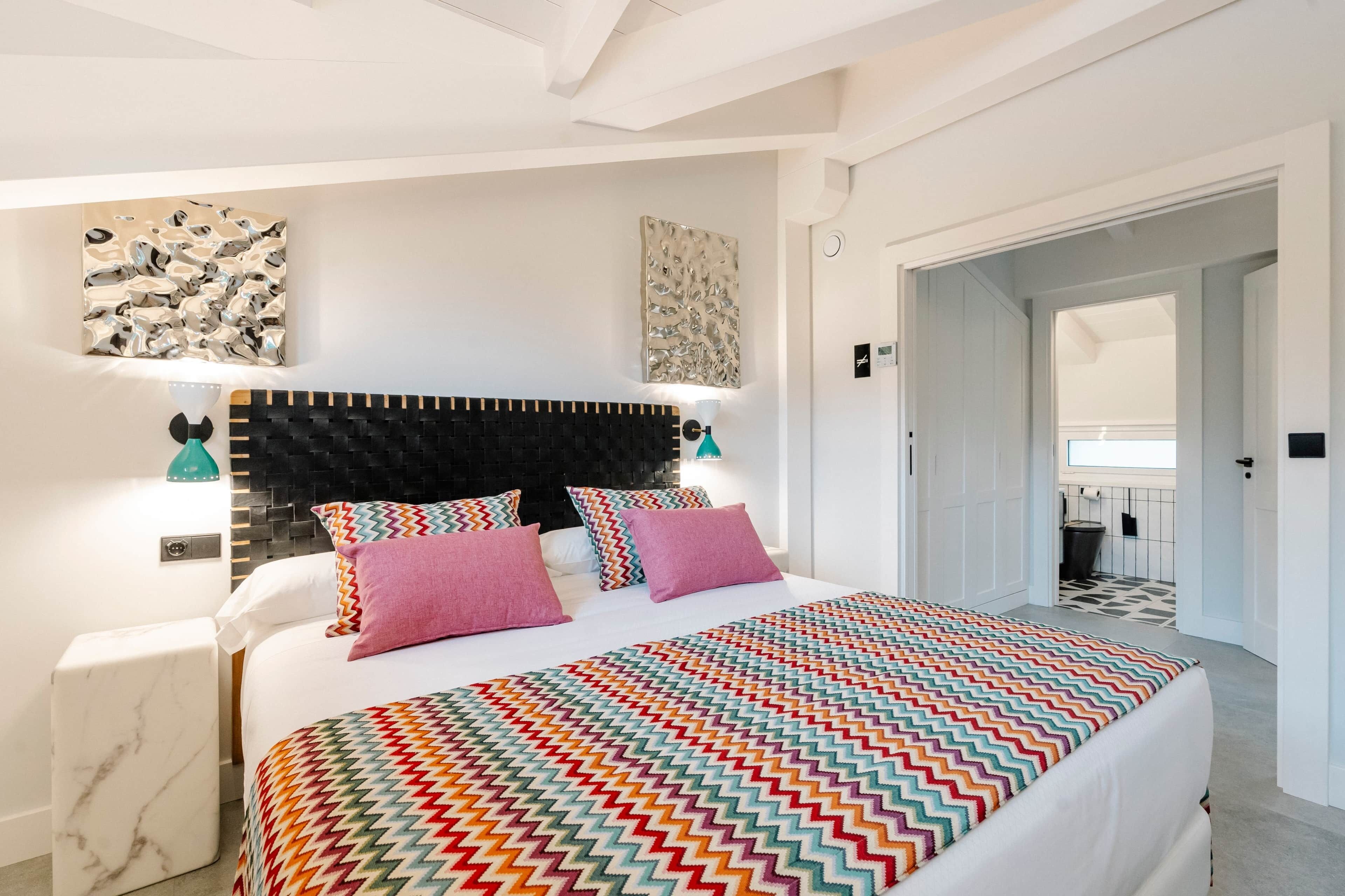 Een moderne slaapkamer met een zwart hoofdeinde, een bed met een kleurrijk zigzagdeken en twee wandlampen.