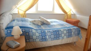 Ein Schlafzimmer mit einem Bett, einem Nachttisch, einer Lampe, einer Fernbedienung und einem Fenster mit Vorhängen.