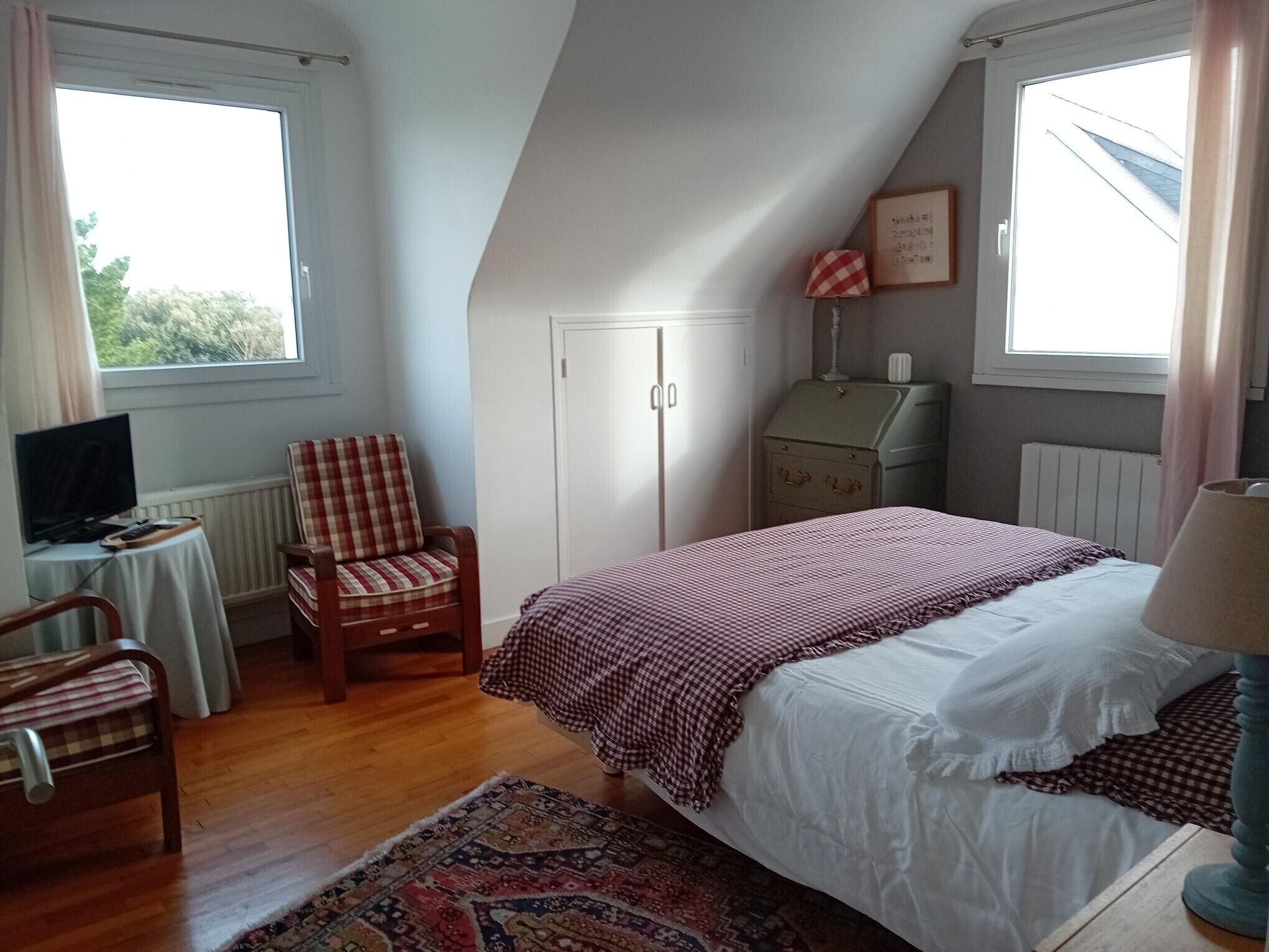 A bedroom with a bed, a chair, a television, a radiator, and a window.