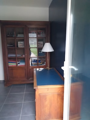 Ein Zimmer mit einem Holzkabinett mit Glastüren, einem blauen Tisch und einer Lampe.
