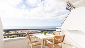 A balcony with a table and chairs, a potted plant, and a view of the sea and buildings. - Club Atlantis nice sea & pool view (Costa Adeje)