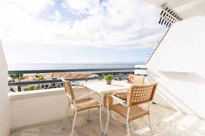 Ein Balkon mit Tisch und Stühlen, einem Blumentopf und Blick auf das Meer und die Gebäude.