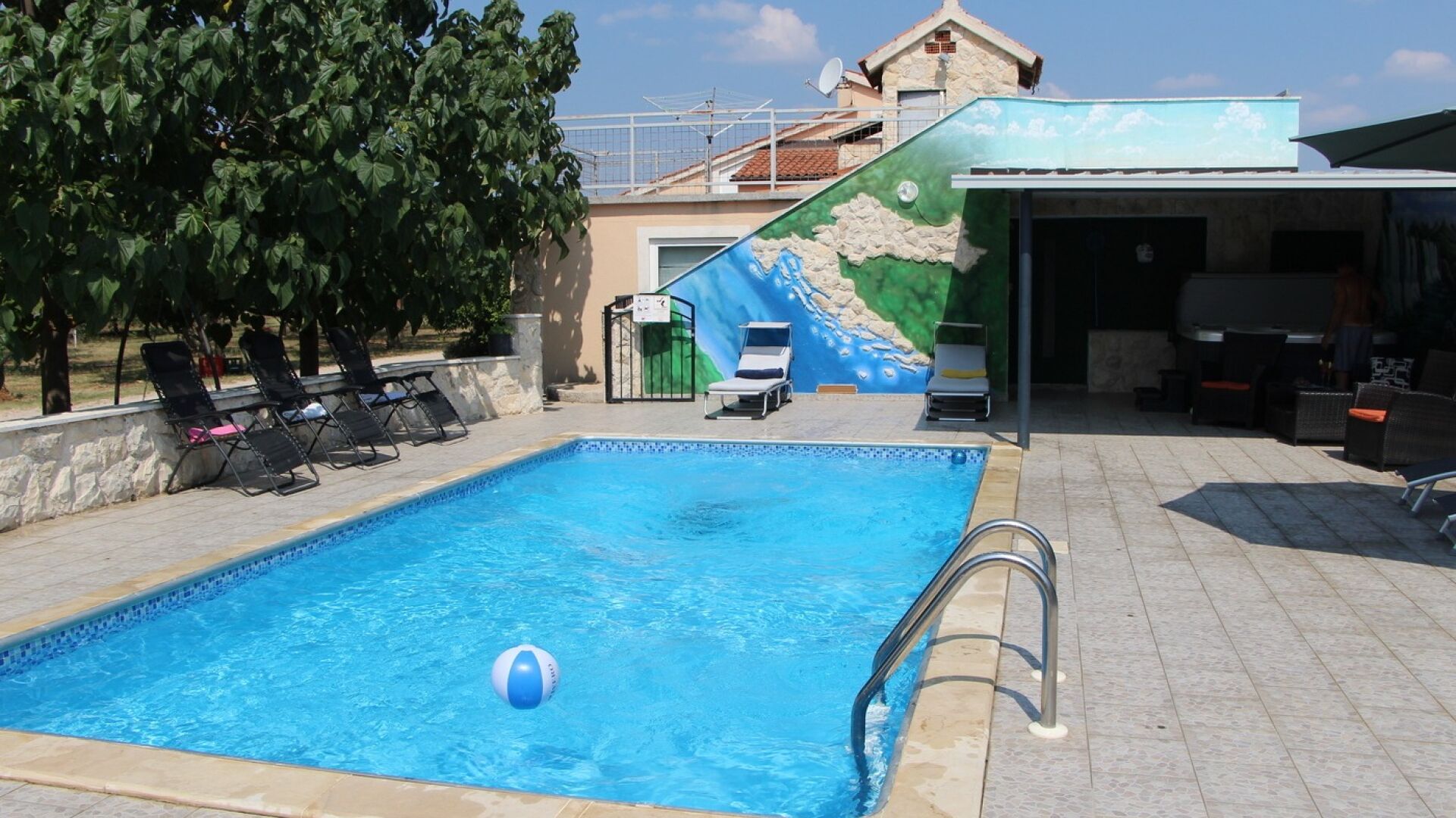 A swimming pool with lounge chairs, a beach-themed mural, and a covered area with chairs.