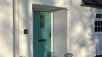 A white building with a teal door, a small window, and a metal container on the ground.