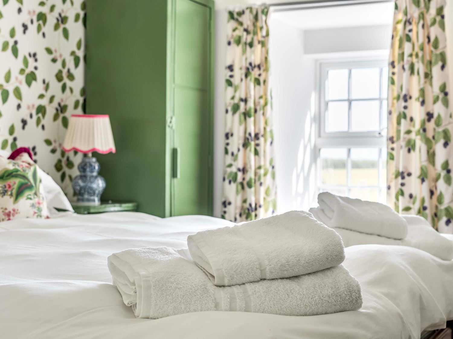 Une chambre d’hôtel avec un lit, une porte verte, des rideaux à motifs floraux et une fenêtre.