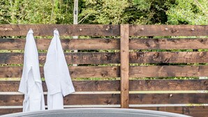 A hot tub with two white towels hanging on a wooden fence. - Bodior Garden Cottage Bach (Holyhead)