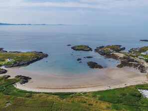 An aerial view of a coastal area with a sandy beach, rocky outcrops, and scattered houses. - Bodior Garden Cottage Bach (Holyhead)
