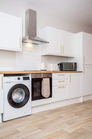 Una cocina moderna con armarios blancos, lavadora, horno y microondas.
