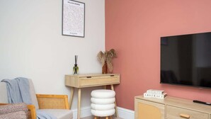 Una habitación con televisión, escritorio, silla, sofá y estantería.