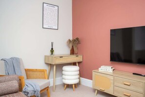 Una habitación con televisión, escritorio, silla, sofá y estantería.