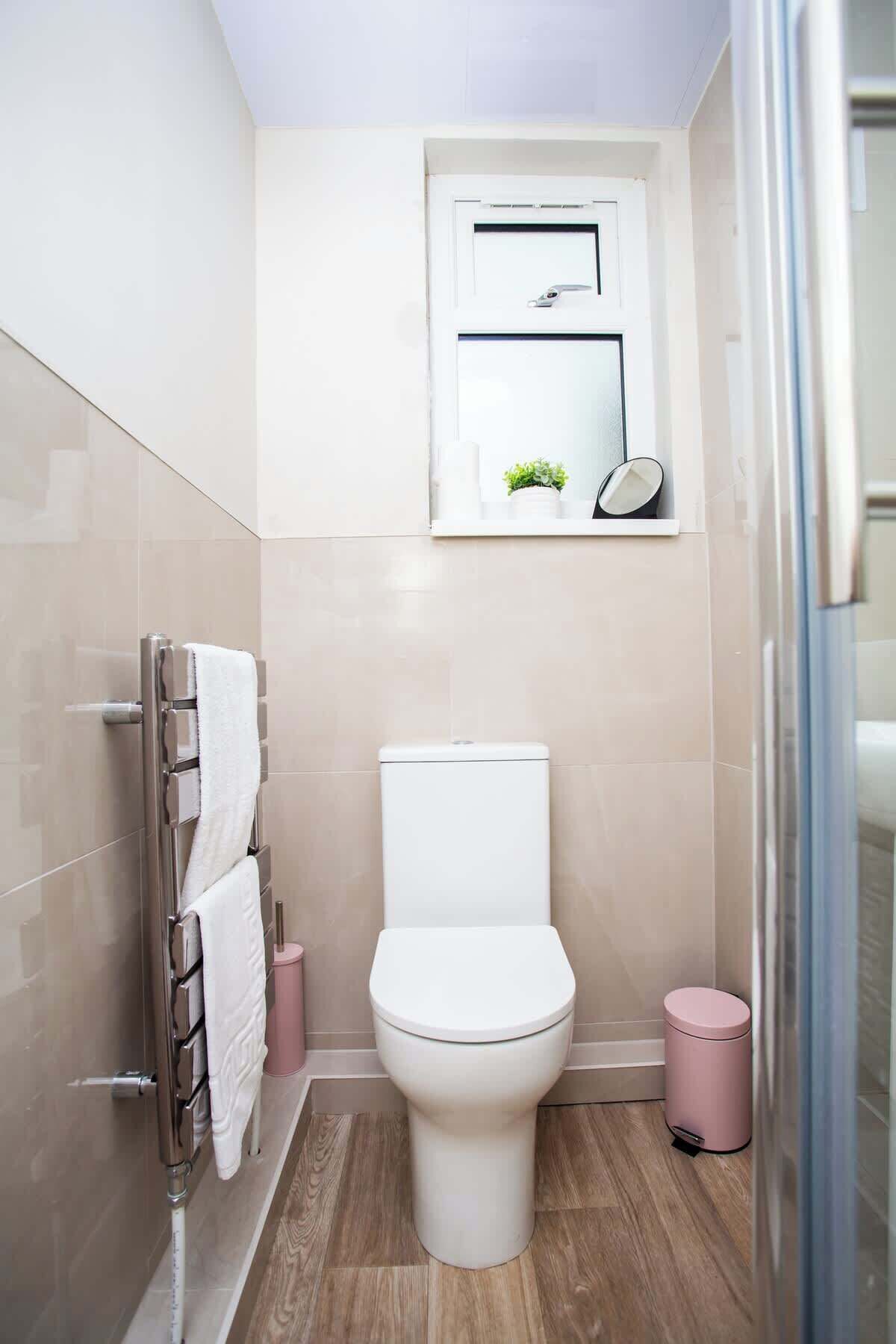 A bathroom with a toilet, a towel rack, a small trash bin, and a mirror.