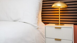 Una cama con ropa de cama blanca y una mesita de noche con lámpara.