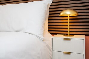 Una cama con ropa de cama blanca y una mesita de noche con lámpara.