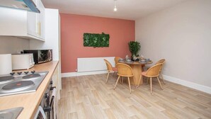 Una cocina moderna con armarios blancos, encimera de madera y comedor con mesa redonda y sillas de mimbre.