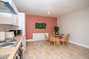 Una cocina moderna con armarios blancos, encimera de madera y comedor con mesa redonda y sillas de mimbre.