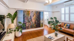 Ett modernt vardagsrum med en stor, abstrakt målning, trägolv, en lädersoffa och diverse krukväxter.