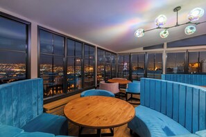 A rooftop bar with blue seating, large windows, and a city view. - Libretto Tbilisi (Tbilisi)
