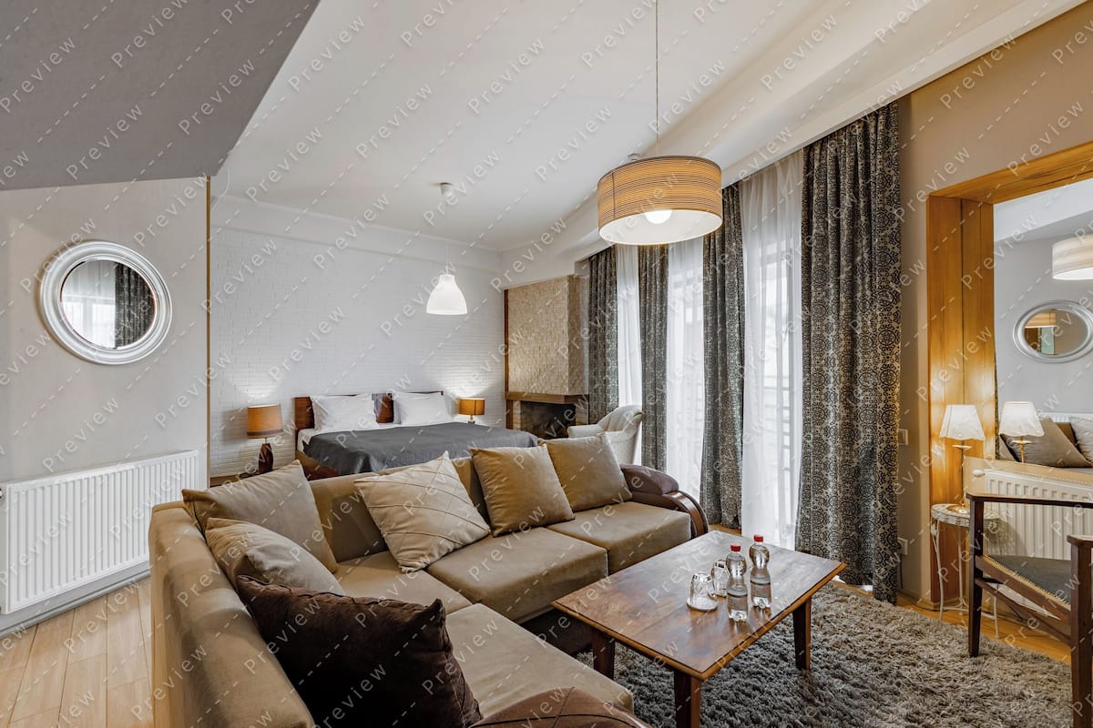 A modern hotel room with a sectional sofa, a wooden coffee table, a round mirror, and a bed with a headboard.
