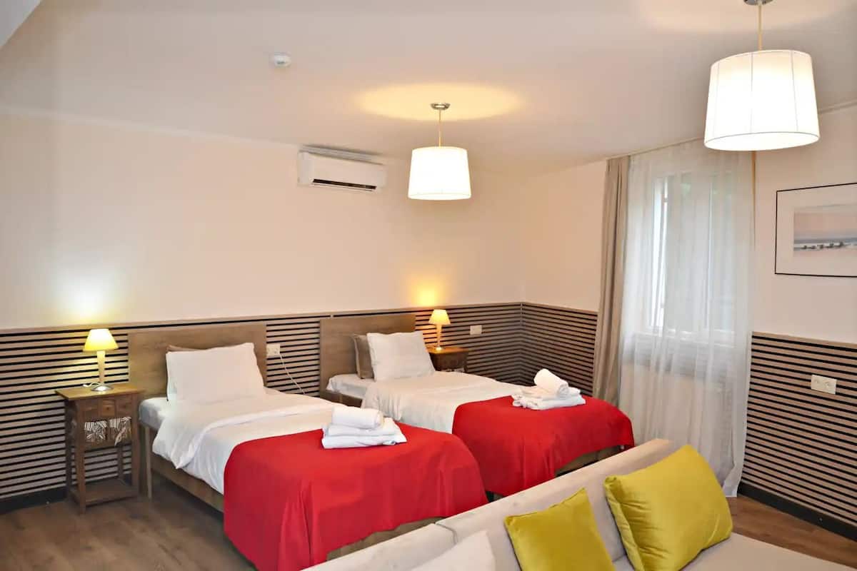 A hotel room with two beds, a sofa, and a large window with curtains.