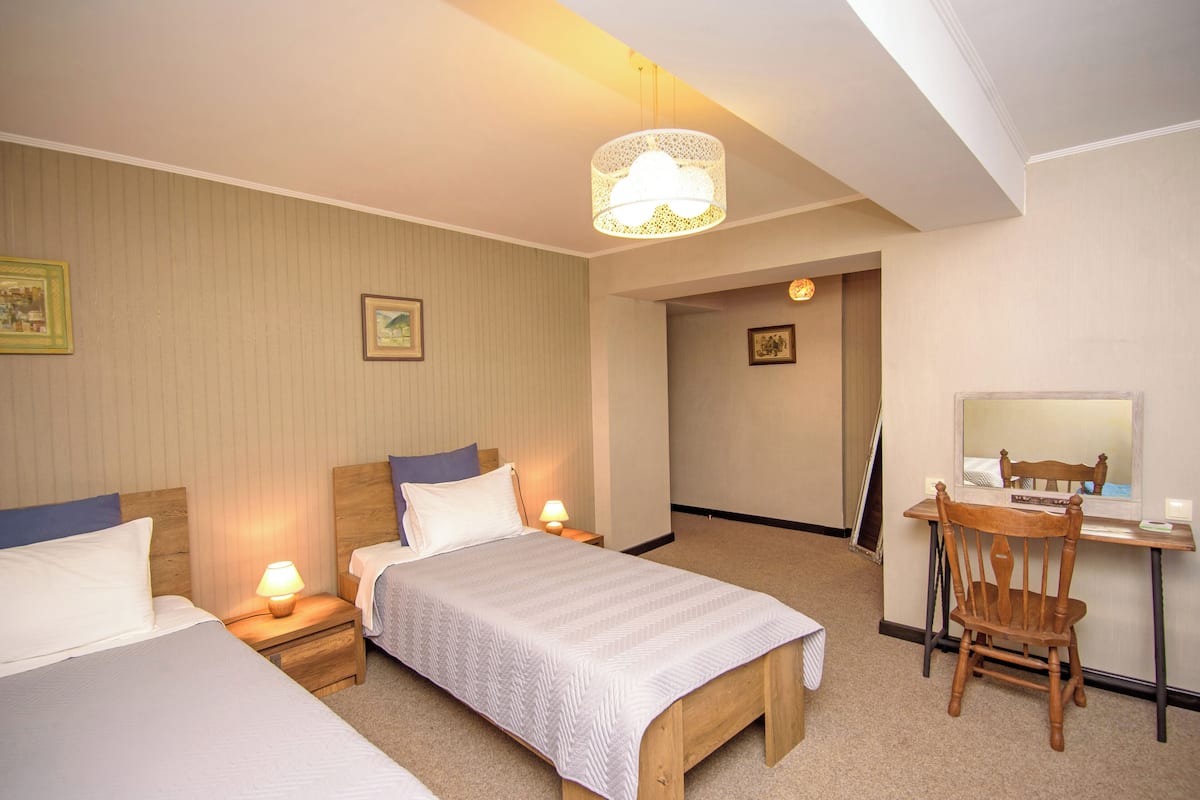 A hotel room with two single beds, a wooden desk with a chair, and a large window.