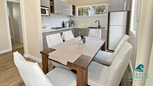 Eine moderne Küche mit weißen Schränken, einer Mikrowelle, einem Kühlschrank und einem Essbereich mit einem Holztisch und weißen Stühlen.