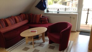 Un salon avec un canapé rouge, un fauteuil rouge, une table basse en bois et un tapis à motifs.