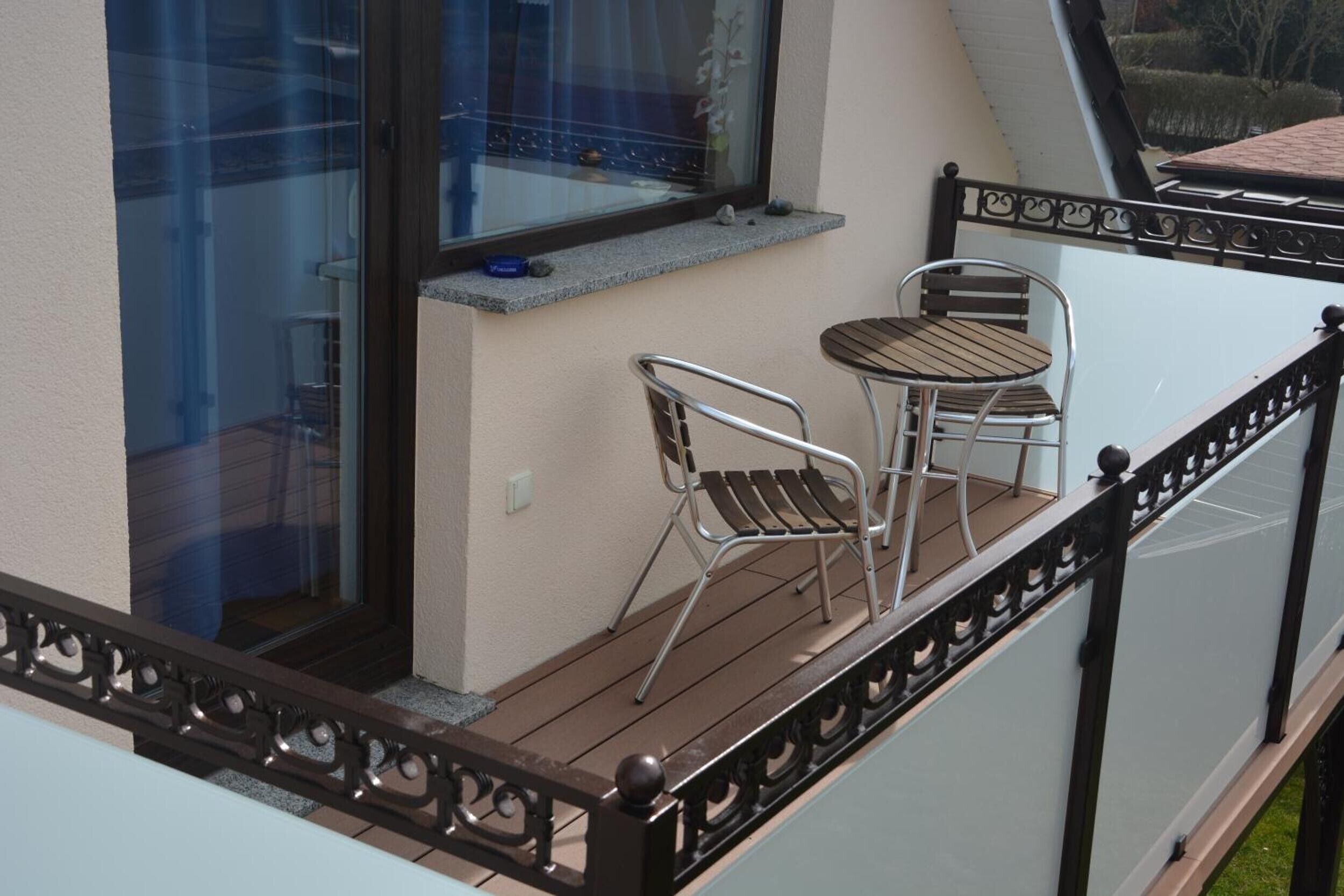 Un balcon avec deux chaises en métal et une petite table, une fenêtre donnant sur l’extérieur et une balustrade décorative.