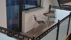 Un balcon avec deux chaises en métal et une petite table, une fenêtre donnant sur l’extérieur et une balustrade décorative.